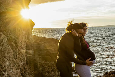 Couple Shooting einer schwangeren frau mit mann, beiu untergehender sonne am meer ; fotografiert von fotoboss.ch